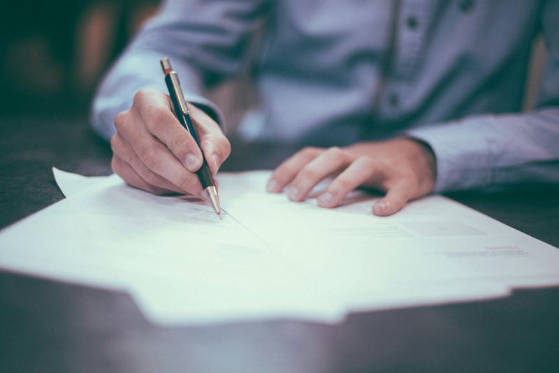 A person signing a document at a desk with a pen