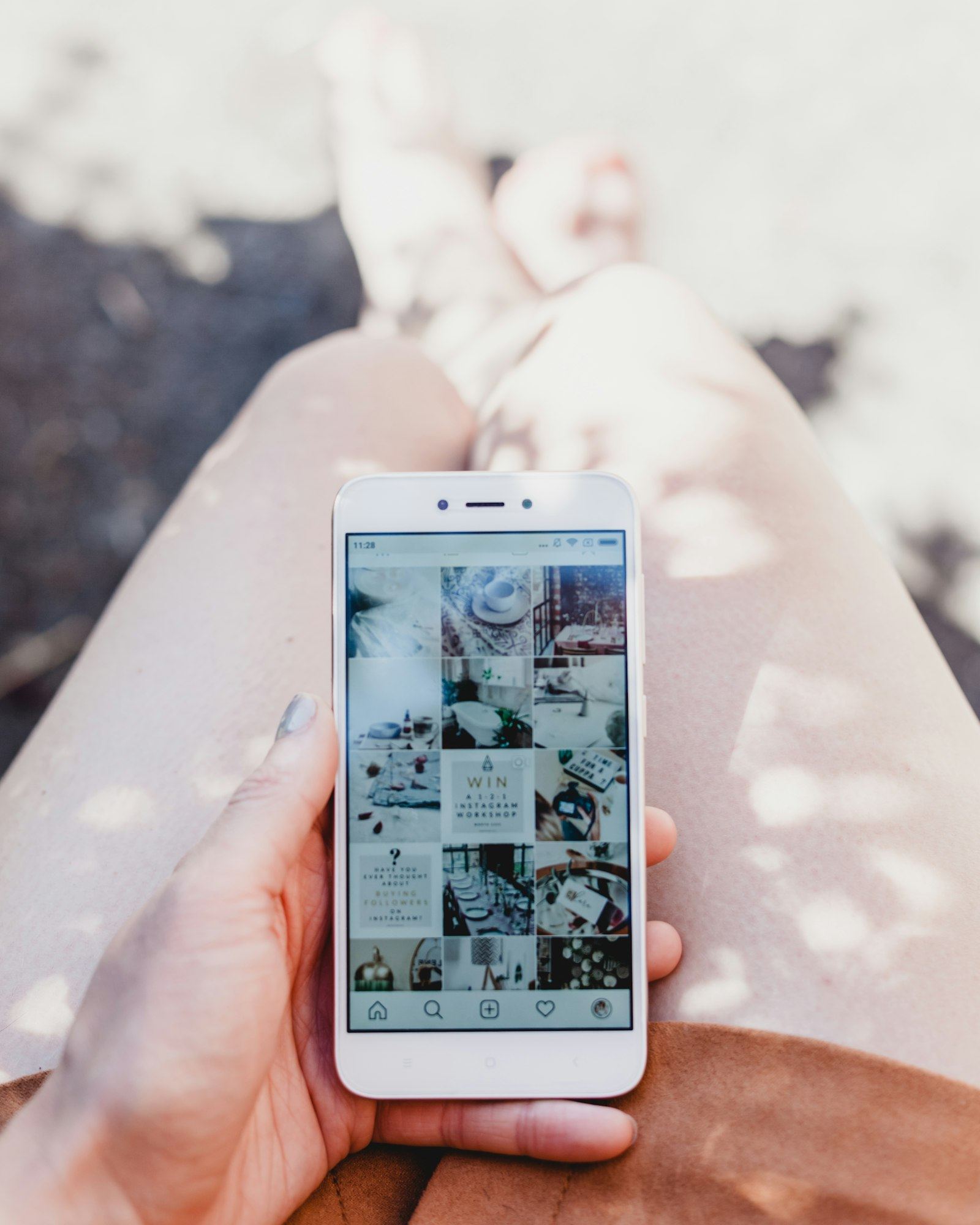 A person holding a white smartphone showing an Instagram feed in bright sunlight