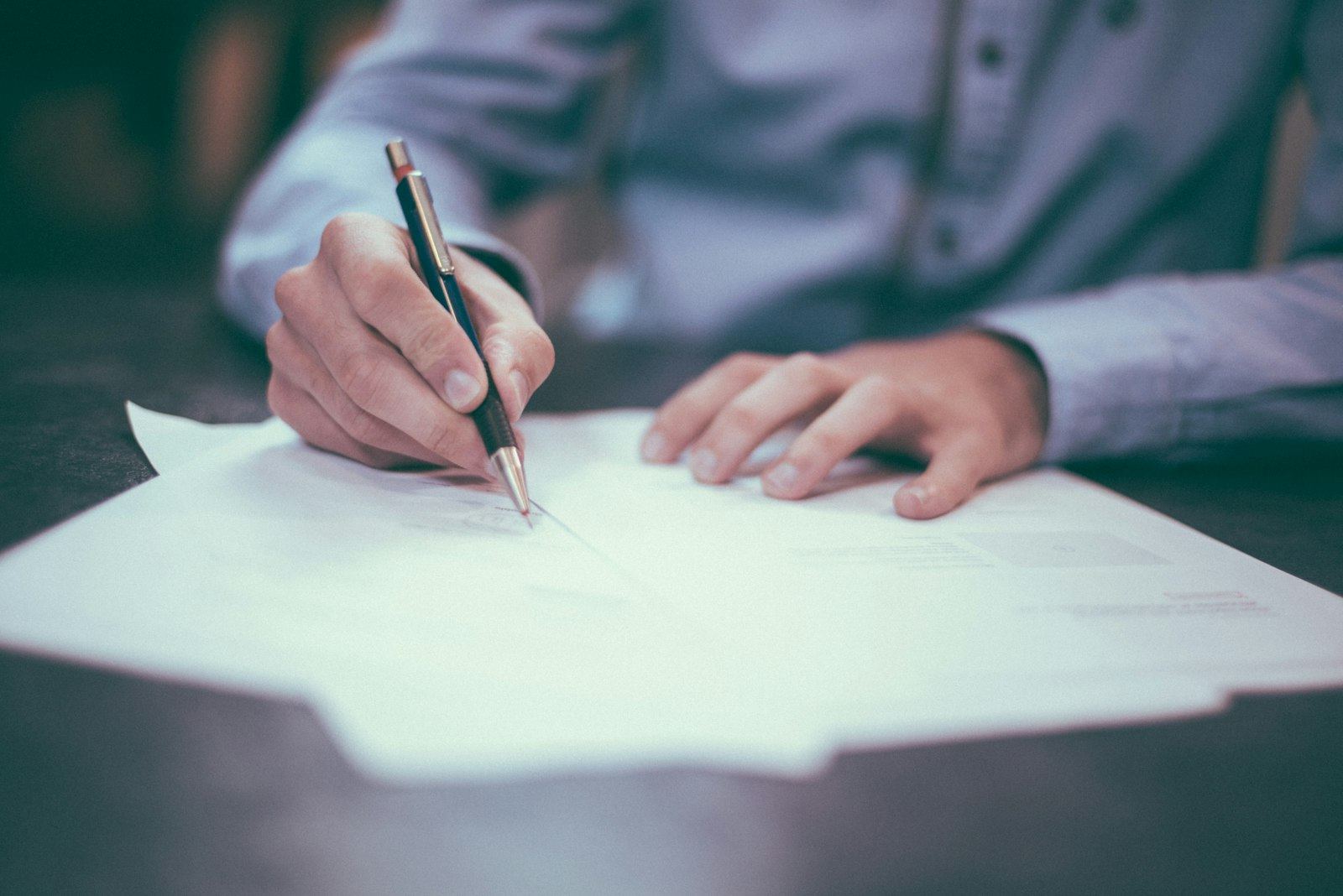 A pair of hands signing a document with a pen on a desk